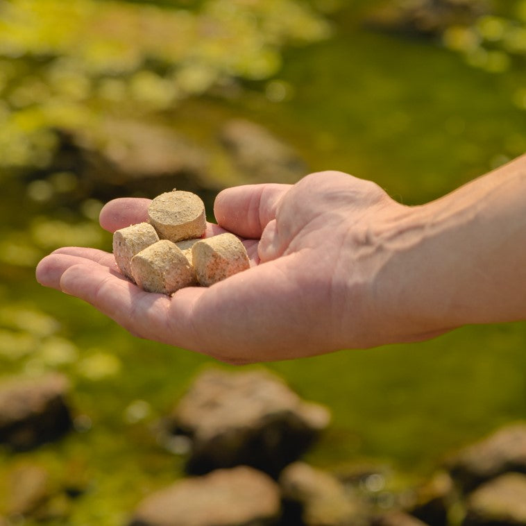 Kasco Macro-Zyme water-soluble bag held in hand at pond edge